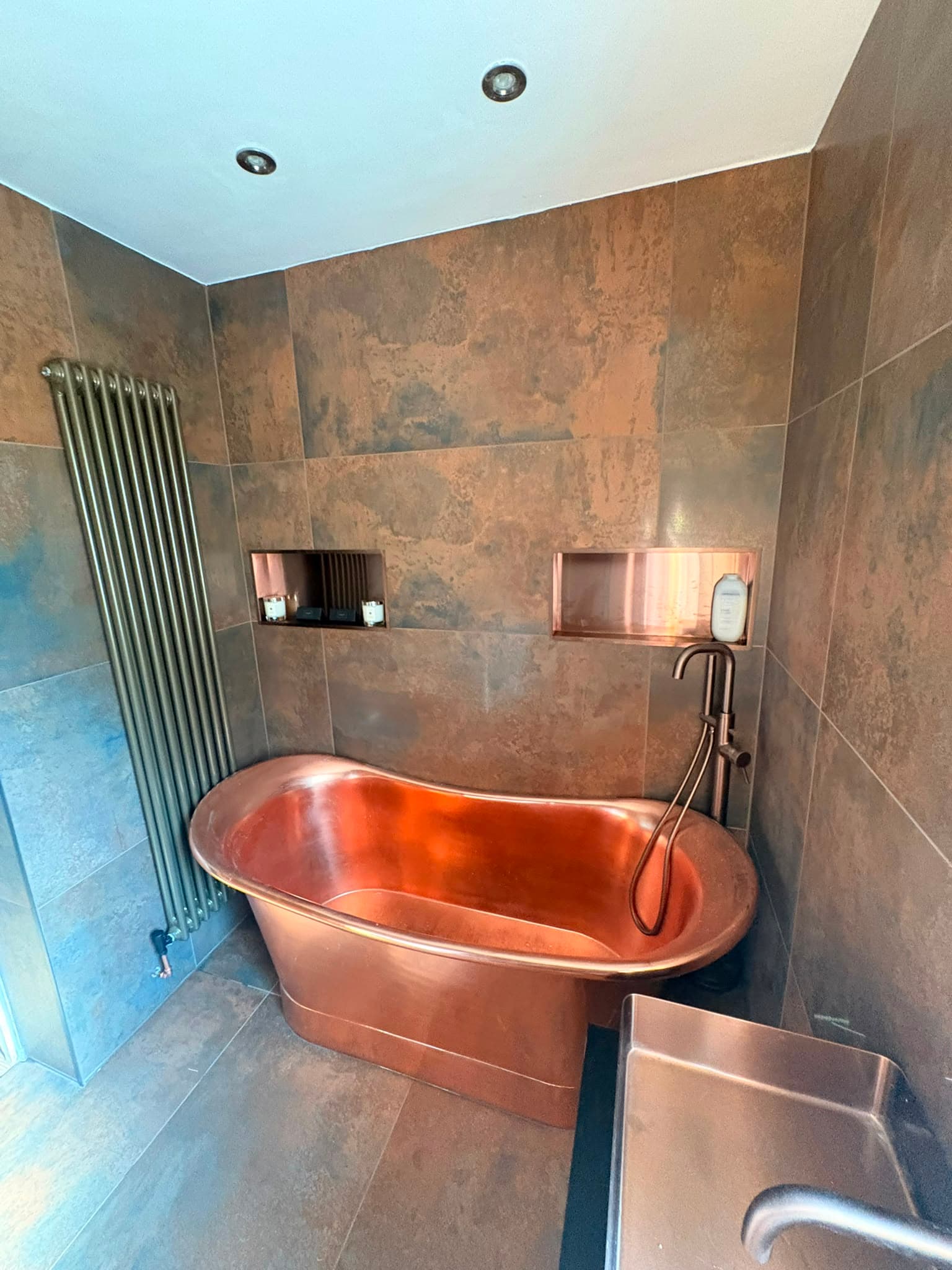 Copper freestanding bath with bronze-effect tiling fitted by WMC Property Maintenance
